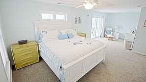 Une chambre à coucher comprenant un lit, une table de chevet, une commode, un ventilateur de plafond et une fenêtre.