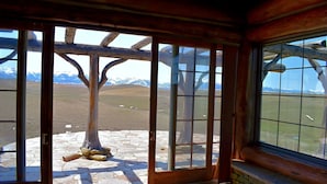 A wooden-framed door with a stone-paved entrance leading to a view of snow-capped mountains. - Glass Cottage Overlooking Beartooth Mountain Range (Roberts)
