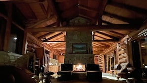 A log cabin interior with a fireplace, wooden beams, stone walls, and a stone floor. - Glass Cottage Overlooking Beartooth Mountain Range (Roberts)