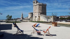 Een historisch kasteel met een vlag, een strandgedeelte met ligbedden en een heldere lucht.
