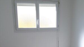 Een slaapkamer met een bed, twee bedlampen, een raam en een klein krukje.