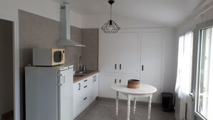 Een keuken met witte kastjes, een magnetron, een fornuis en een hangende lamp.