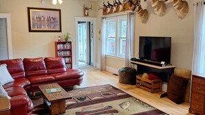 Una sala de estar con un sofá de cuero rojo, un televisor de pantalla plana, cráneos de animales montados y un ventilador de techo.