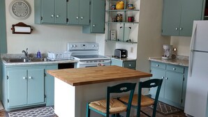 Una cocina con armarios azul verdoso, una mesa de madera y dos sillas de mimbre.