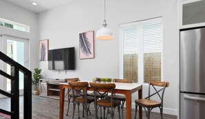 A modern kitchen with a dining area, a TV mounted on the wall, and a staircase leading to another level.