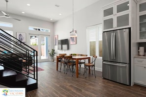 A modern kitchen with a stainless steel refrigerator, wooden dining table, and chairs. - Coastal Getaway for 12 | Private Pool + Beach Access (South Padre Island)