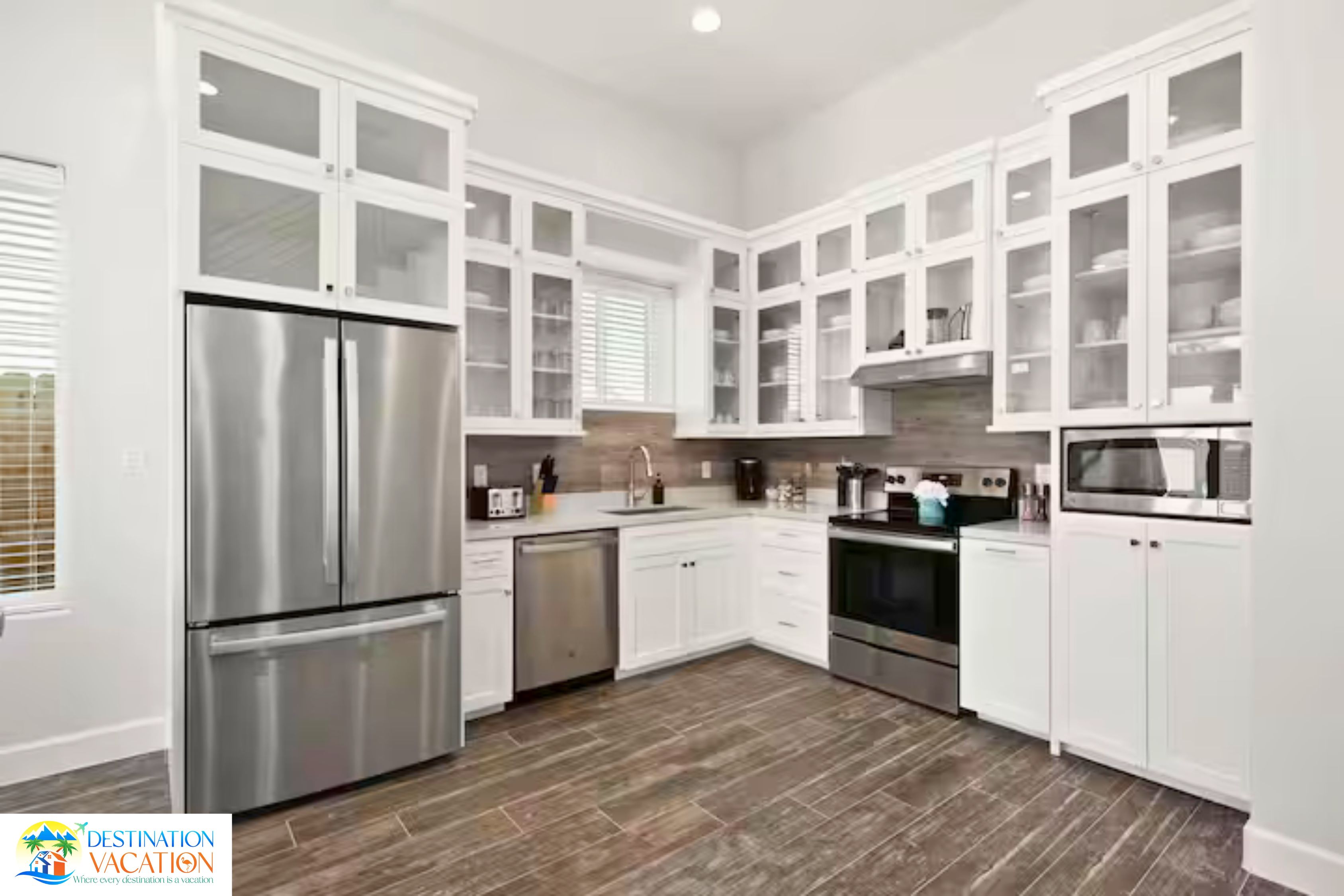 A modern kitchen with white cabinetry, stainless steel appliances, and a wooden floor.