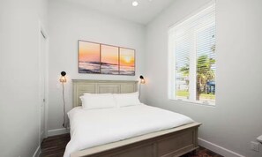 A bedroom with a bed, a painting, and a window with blinds.