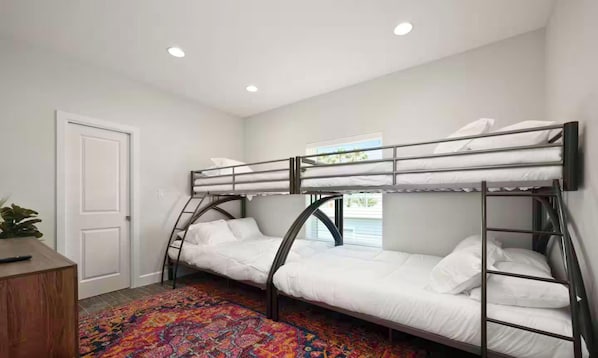Een kamer met stapelbedden, een deur, een raam en een kleurrijk vloerkleed.