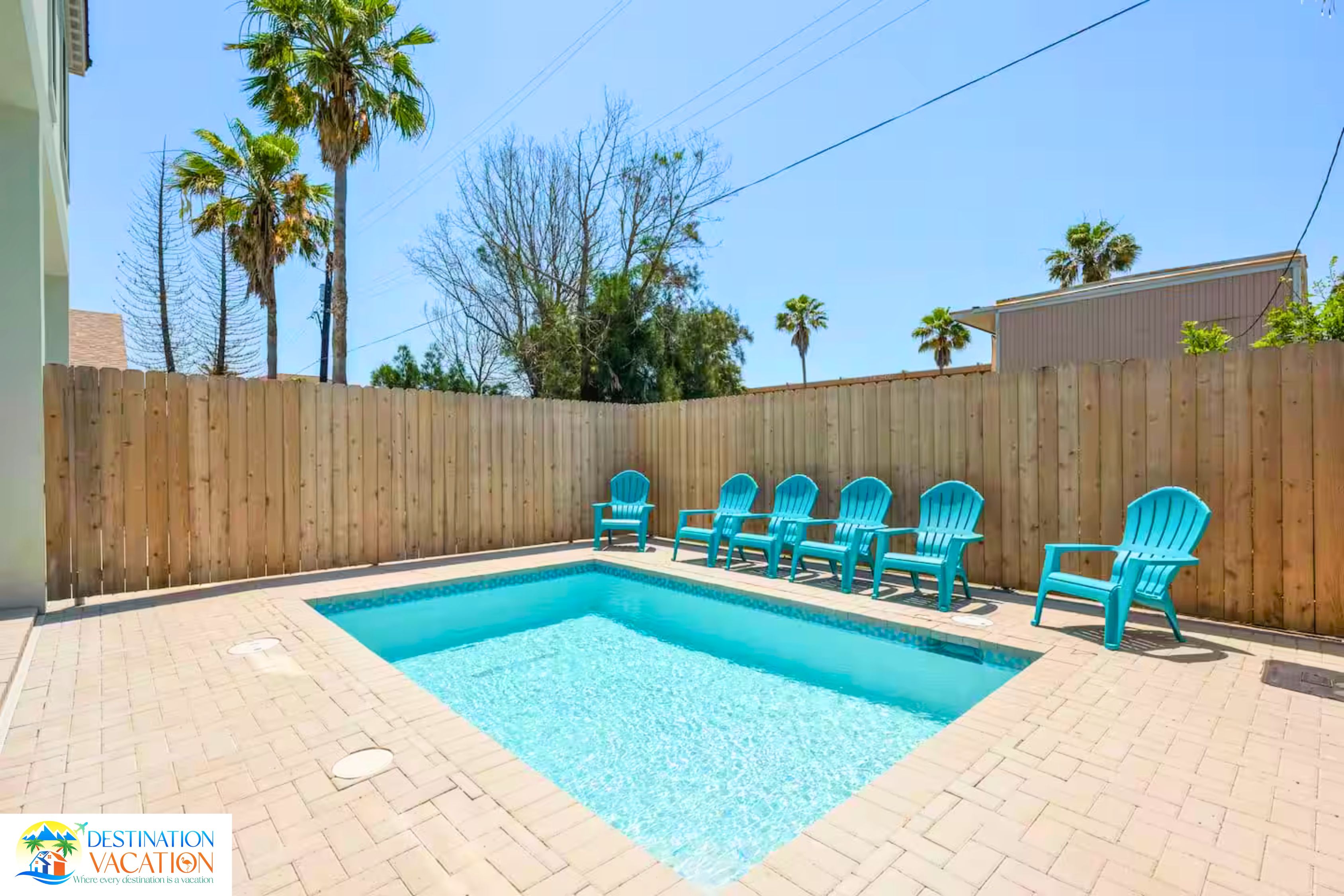 Une piscine rectangulaire entourée d’une clôture en bois, avec plusieurs chaises bleues disposées autour de la piscine.