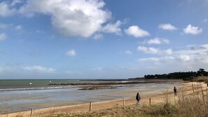 Ein Strand mit zwei Personen, die im Sand stehen, wolkenlosem Himmel und ruhiger See.