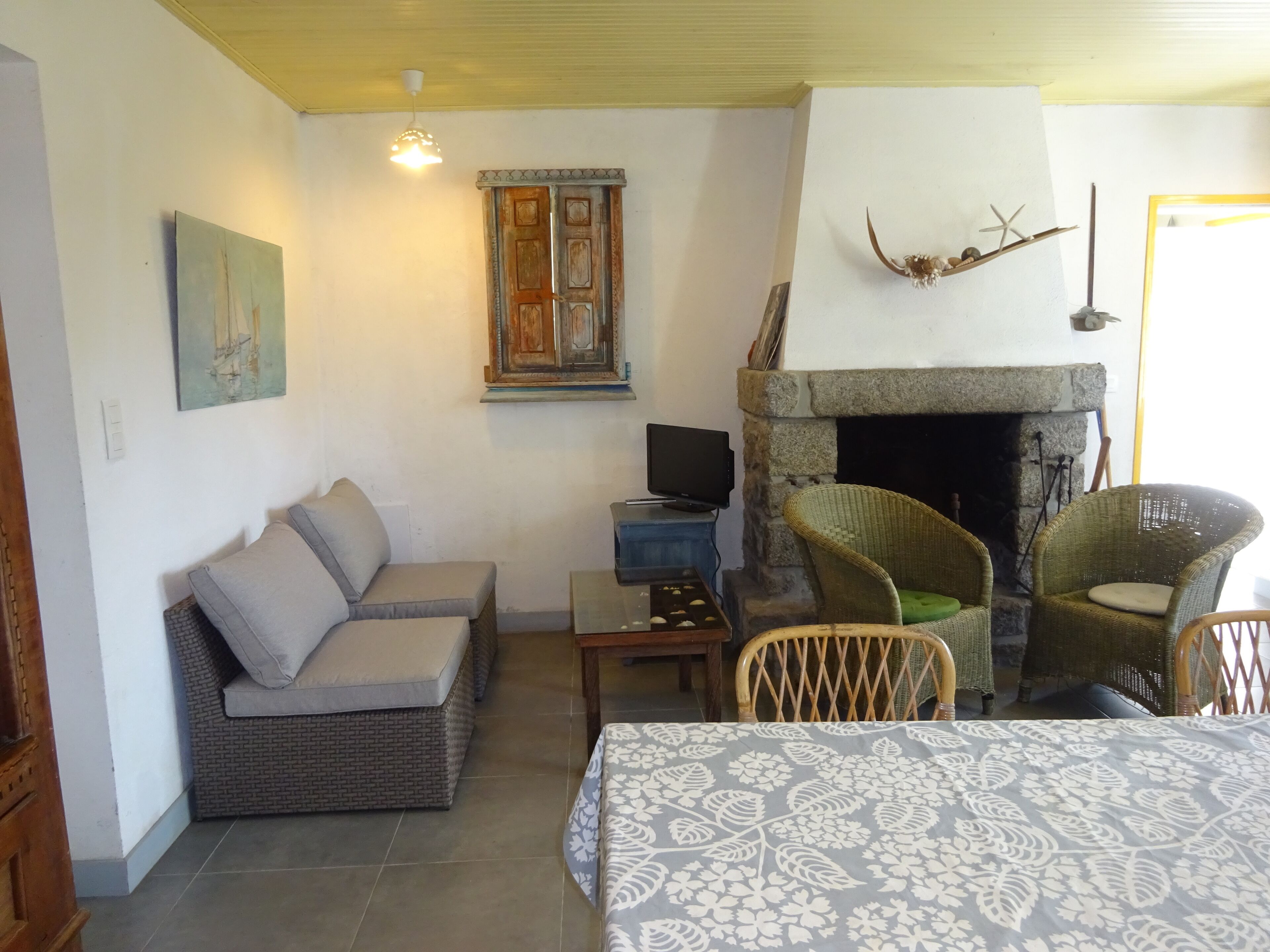 Un salon confortable avec un canapé, deux fauteuils en osier, une cheminée et un téléviseur.