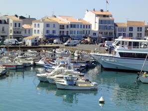Un port de plaisance où sont amarrés différents bateaux, un bâtiment blanc surmonté d’une marquise bleue et un drapeau au sommet.