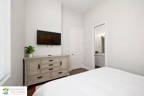 A bedroom with a bed, dresser, TV, and a door leading to a bathroom. - HUGE South Padre Retreat | 8BR | 2 Pools | Near Beach (South Padre Island)