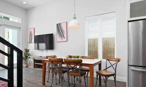 A modern kitchen with a dining area, stainless steel appliances, and a large window with blinds.