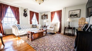 A living room with a sofa, armchair, wooden coffee table, and patterned rug. - The Clipper - 1747 Historic Isaac Pierce House 1st Floor (Somerset)