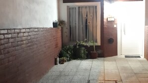 A narrow outdoor corridor with a tiled floor, a brick wall on one side, and a door at the end.