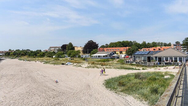 En strand med sandet bredde, et par personer og bygninger i baggrunden.