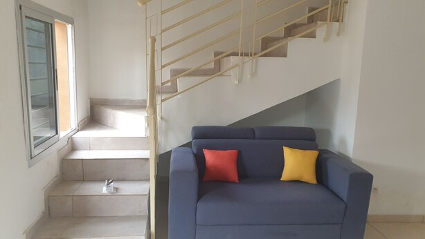 Eine Treppe mit Handlauf, ein blaues Sofa mit zwei Kissen und ein Fenster mit Jalousien.