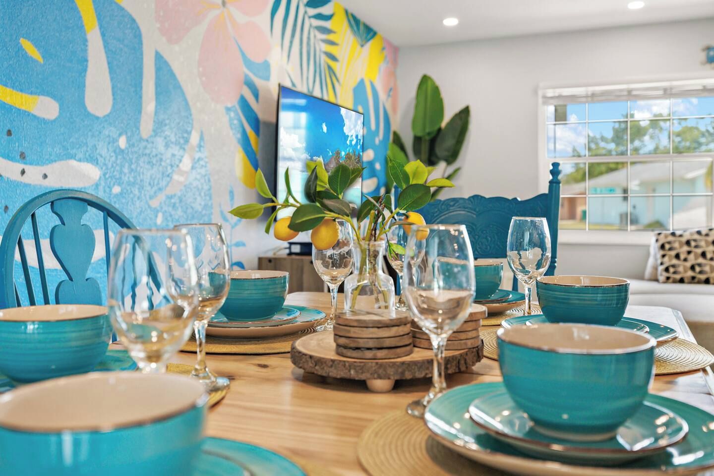 A dining table set with blue bowls and wine glasses, surrounded by wooden coasters and a decorative plant with lemons.
