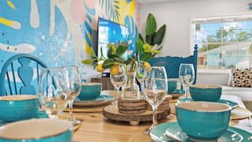 Een gedekte eettafel met blauwe kommen en wijnglazen, omringd door houten onderzetters en een decoratieve plant met citroenen.
