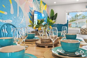 A dining table set with blue bowls and wine glasses, surrounded by wooden coasters and a decorative plant with lemons.