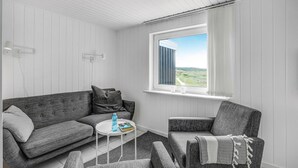 A room with a grey sofa, a grey armchair, a small white table, and a window with a view of greenery. - Cozy home in Thisted with WiFi (Thisted)
