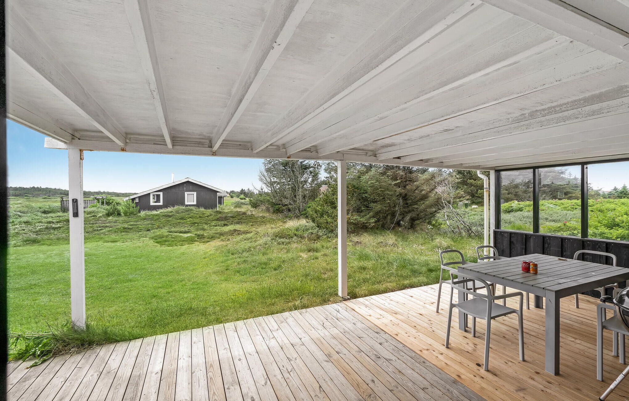 An outdoor patio with a table and chairs, overlooking a grassy area and a house.