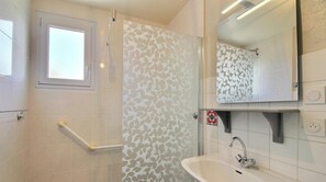 A bathroom with a shower, a window, a sink, and a mirror.