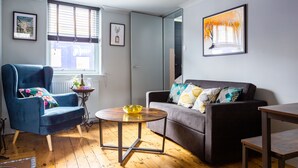 A living room with a blue armchair, a grey sofa, a round coffee table, and a framed picture on the wall. - Cheerful Cottage in the Heart of Brighton (Brighton)