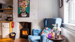 A cozy living room with a fireplace, a blue armchair, and a table with a bottle and glasses. - Cheerful Cottage in the Heart of Brighton (Brighton)