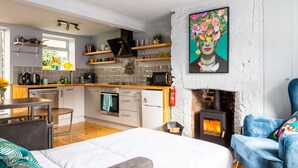 A modern kitchen with a fireplace, a dining area, and a living space with a sofa and a painting. - Cheerful Cottage in the Heart of Brighton (Brighton)