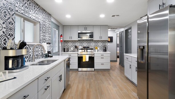 Cozinha moderna com armários cinzas, eletrodomésticos de aço inoxidável e azulejos de backsplash estampados.