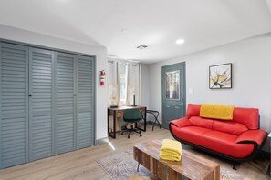 A room with a red sofa, a wooden coffee table, a desk with a chair, a wardrobe, and a door with a window. - 30+ Days, Dog Friendly, Playground, Covered Parking, Hot Tub, Huge Yard. (Phoenix)
