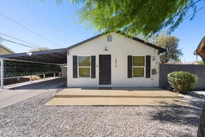 A single-story house with a dark front door, a small porch, and a gravel driveway. - 30+ Days, Dog Friendly, Playground, Covered Parking, Hot Tub, Huge Yard. (Phoenix)