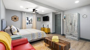 Quarto com cama, sofá vermelho, mesa de centro de madeira, guarda-roupa e televisão na parede.
