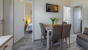Et moderne hotelværelse med spiseplads, fjernsyn monteret på væggen og udsigt til det tilstødende soveværelse.