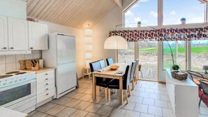 A modern kitchen with white cabinets, a stove, and a refrigerator. There is a dining area with a table and chairs, and a large window offering a view of the outdoors. - 1 bedroom lovely home in Bolmsö (Bolmsö)