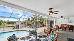 Un espace piscine extérieur doté de tables en verre et de chaises en osier, d’un patio couvert et offrant une vue sur un quartier résidentiel.