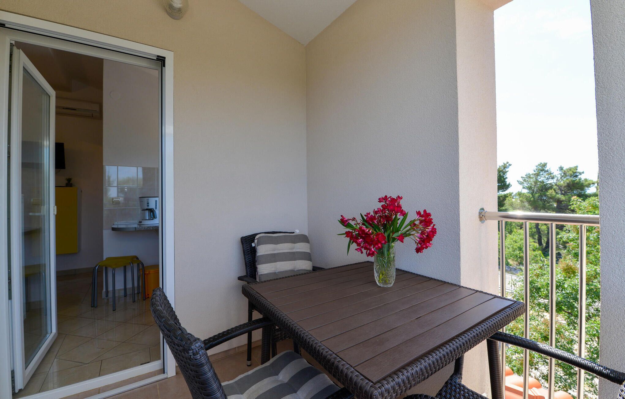 A balcony with a wooden table, wicker chairs, and a vase of red flowers.