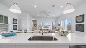 A modern kitchen with a central island, white cabinetry, and pendant lighting. - 88° GAS Heated Pool, 85" TV, 3 King Beds, Steps to Beach, Arcade, Shuffleboard (Gulf Shores)