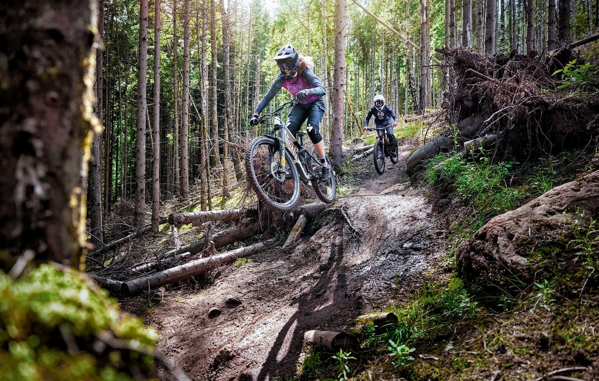 Sentiero nella foresta con due mountain biker che percorrono un tratto fangoso.