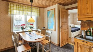 Une pièce chaleureuse avec une table à manger en bois, des chaises, une carte accrochée au mur et un lit près d’une fenêtre.