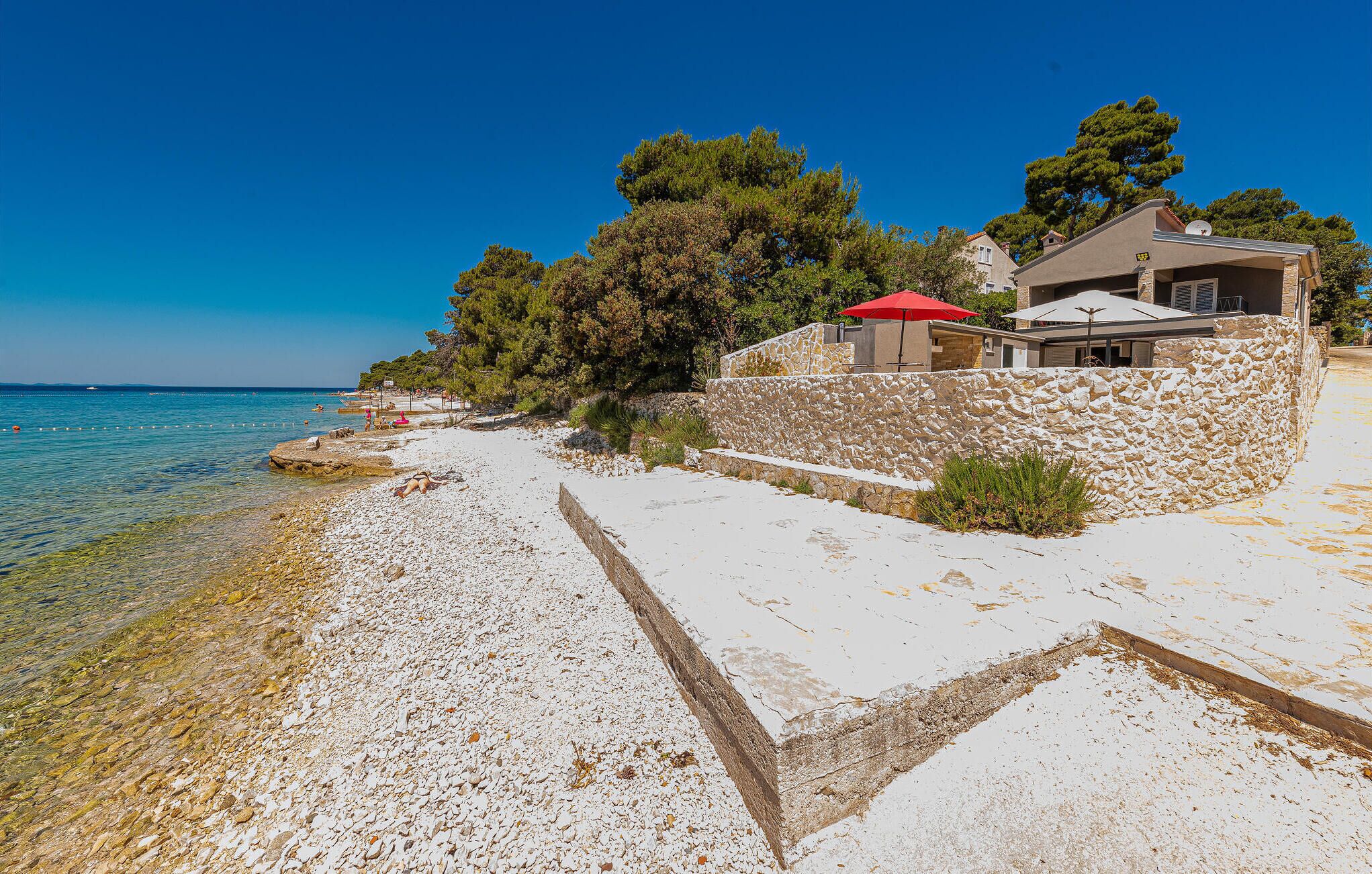 A coastal property with a stone wall, a red umbrella, and a clear view of the sea.