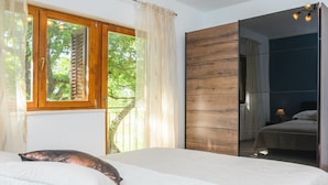 Une chambre avec un grand lit, une fenêtre avec des volets en bois et une vue sur la verdure.