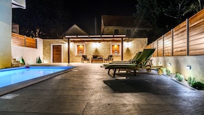 Un espace aménagé au bord de la piscine, avec une terrasse en pierre, des chaises longues et un mur en pierre.