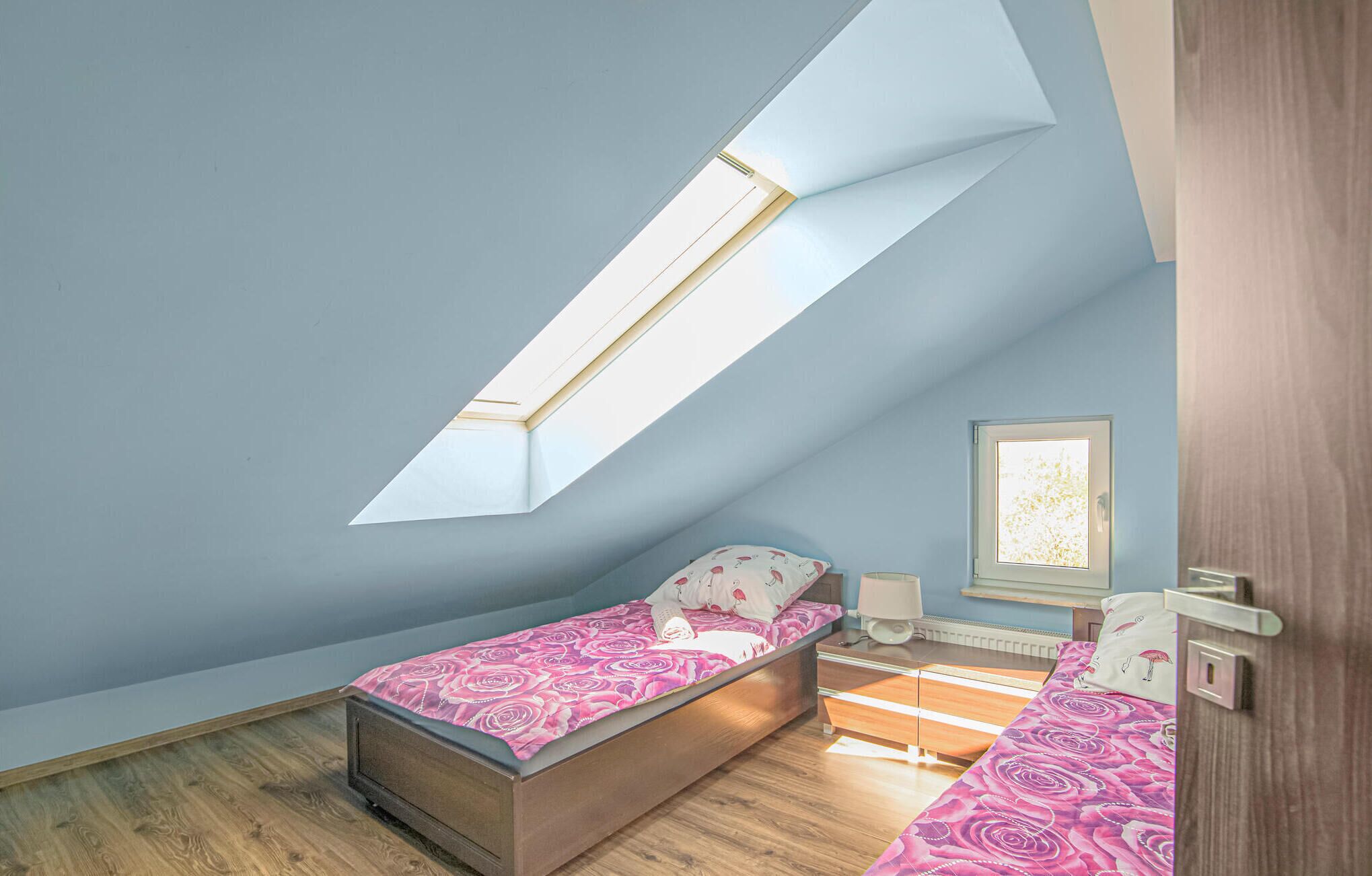 Une chambre avec une lucarne, un lit, une table de chevet et un miroir.