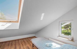 A small, bright room with a sloped ceiling, a single bed, a window with a view of greenery, and a radiator.