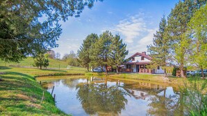 A house with a pond in front, surrounded by trees and a grassy area.