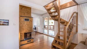 A spacious living area with a wooden staircase, a fireplace, and large windows offering views of the outdoors.